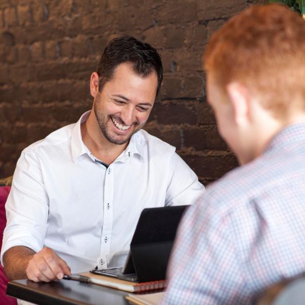 Two men smiling and working on laptop in cafe