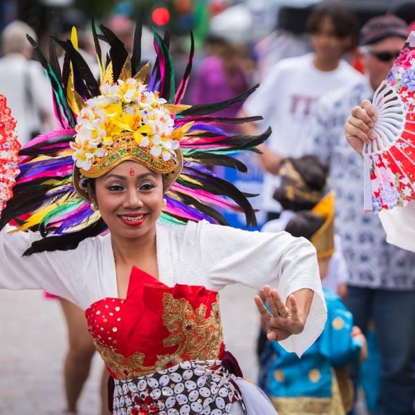 Performer in a vibrant, ornate costume with a feathered headdress and fans, dancing at Maitland Riverlights