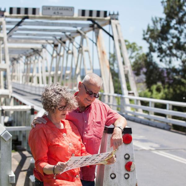 Two seniors looking at a brochure outside near a bridge