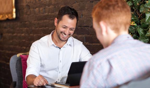 Two men smiling and working on laptop in cafe