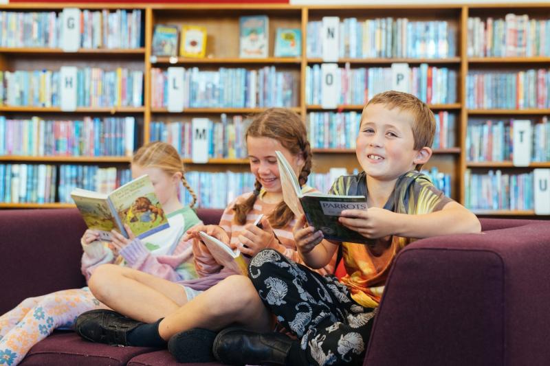 Three kids sitting on a lounge each holding a book in a library