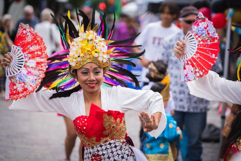 Performer in a vibrant, ornate costume with a feathered headdress and fans, dancing at Maitland Riverlights