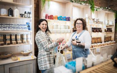 Two females smiling looking at the camera exchanging a shopping in a shop 