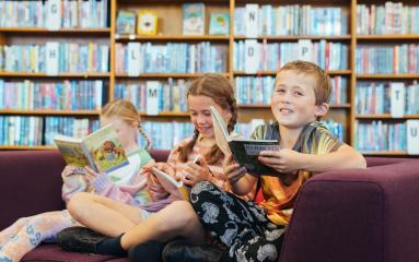 Three kids sitting on a lounge each holding a book in a library