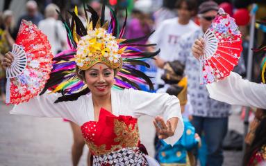 Performer in a vibrant, ornate costume with a feathered headdress and fans, dancing at Maitland Riverlights