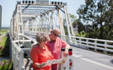 Two seniors looking at a brochure outside near a bridge