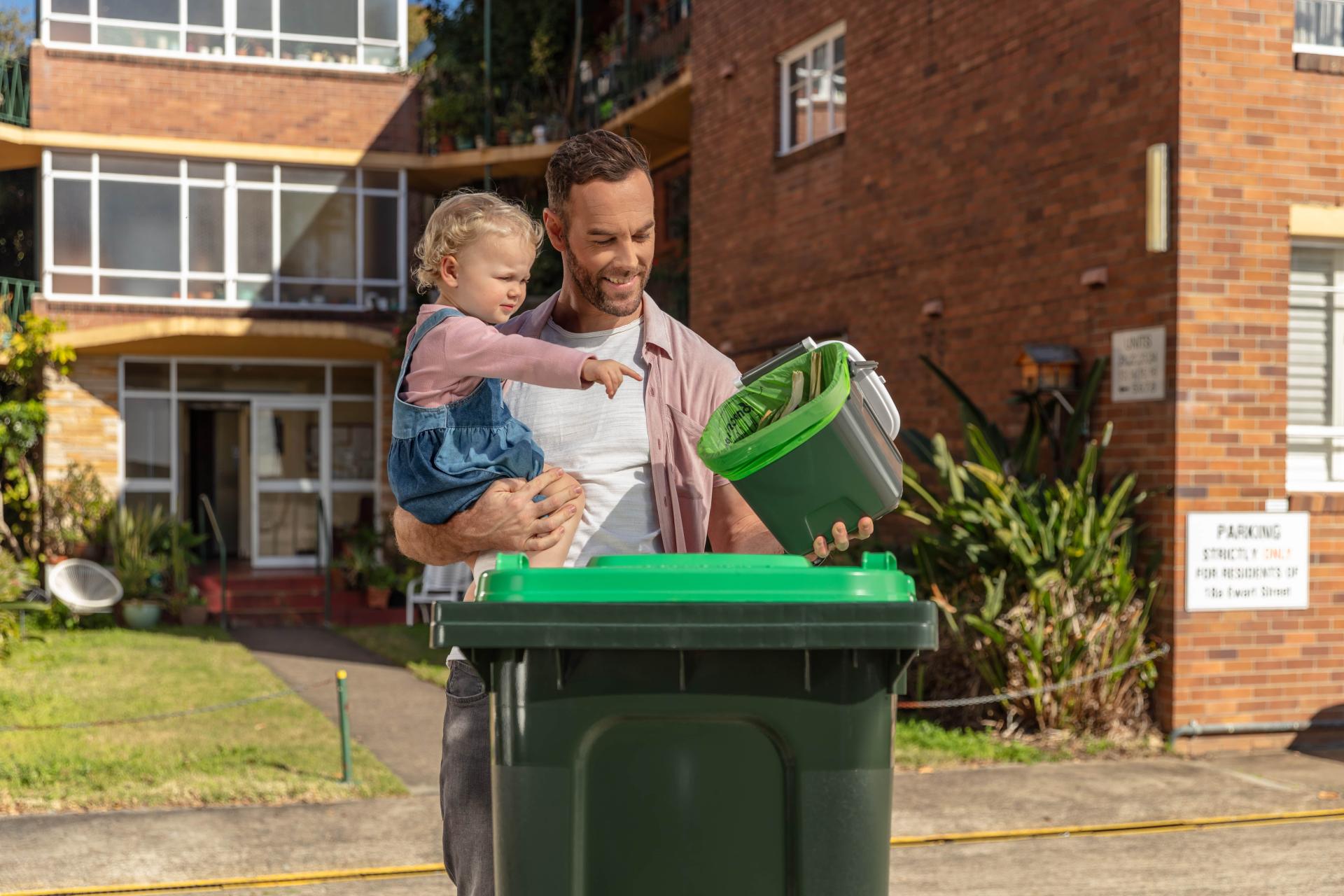 Man and daughter placing food organics in green bin